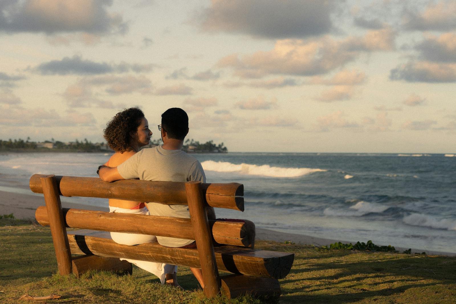 A couple sits on a wooden bench, enjoying a romantic beach sunset.