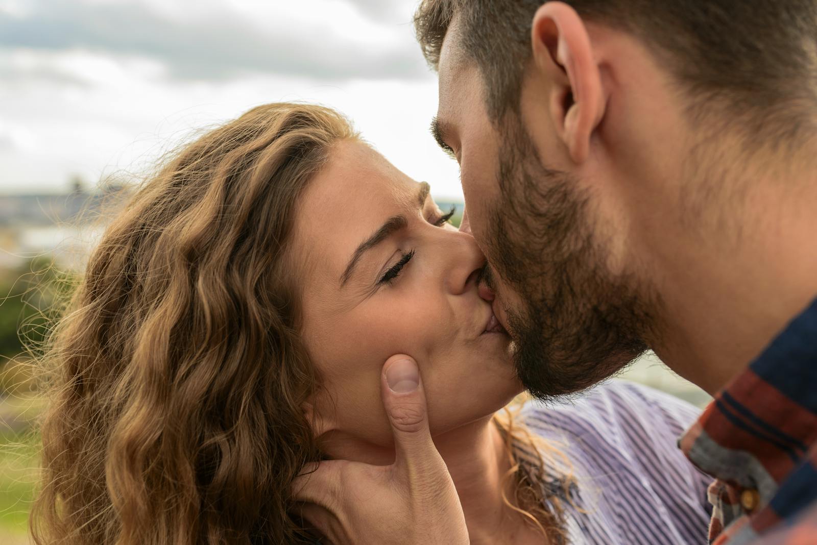 Close-up of a couple sharing a passionate kiss outdoors, capturing a moment of romance and affection.