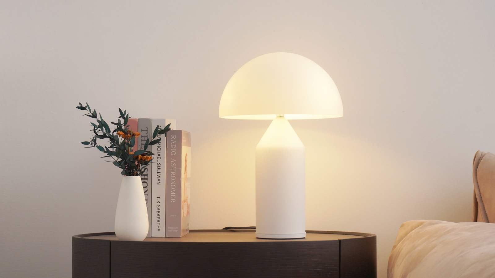 A glowing lamp sits next to a vase and books.
