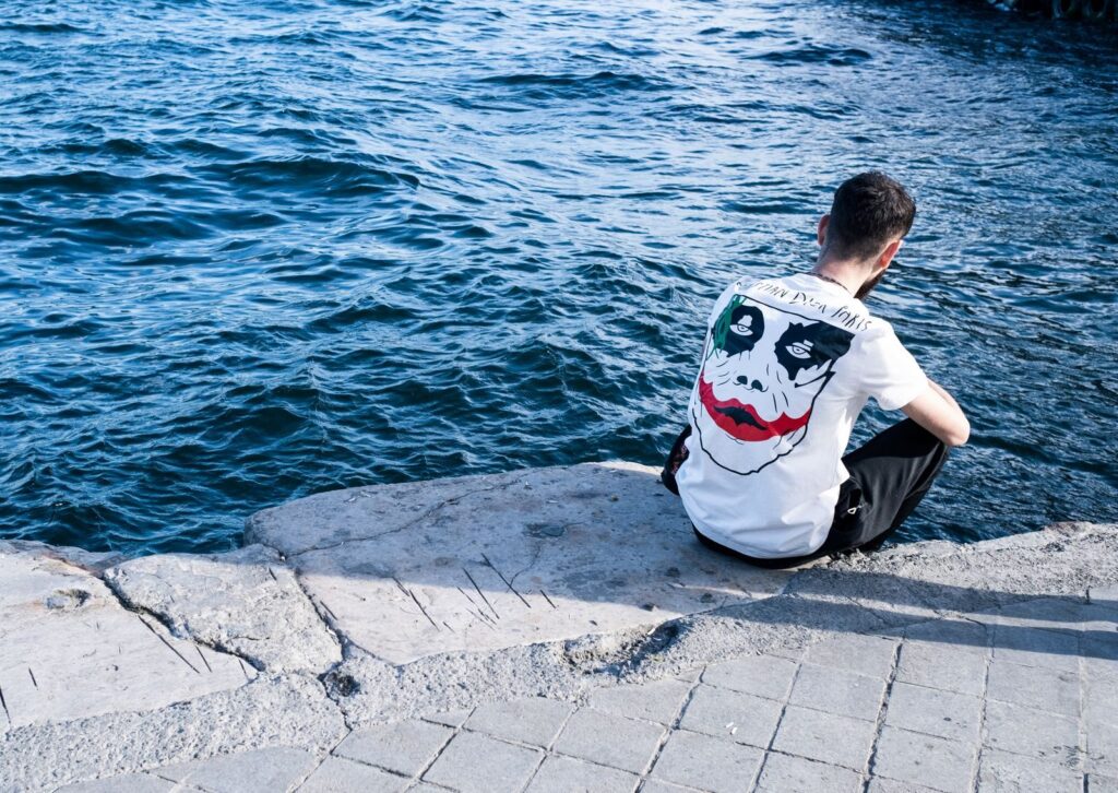 A young man in a white graphic t-shirt sits alone on a concrete pier by the Bosphorus in Istanbul.
